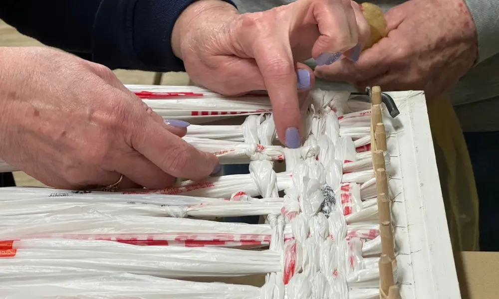 Woman weaving plastic bags into mats for the homeless